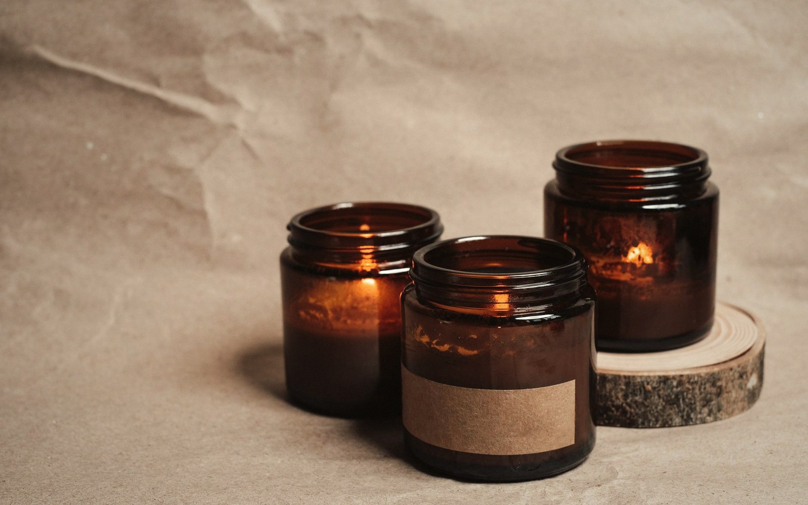 A single amber glass candle jar backlit so the wax is translucent and the wick is a dark vertical line at the centre